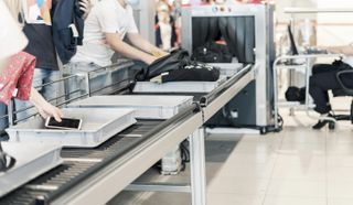 Passengers loading items into security trays in front of the x-ray machine