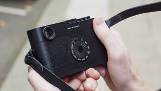 Leica M11-D camera in hand, ISO shutter dial in the background