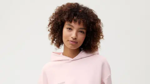 Colorifix/Pangaia Model with short curly hair wearing a pink hoodie.